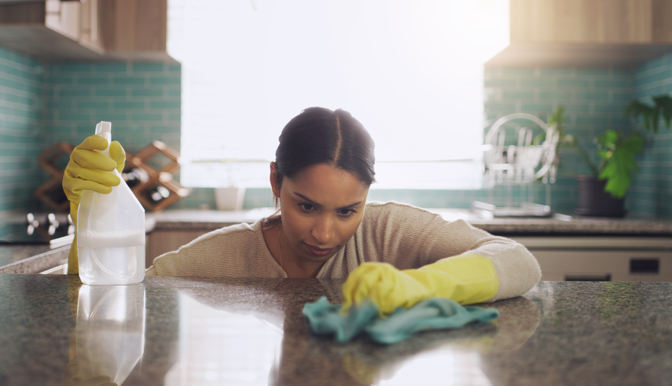 A woman looking closely at granite countertop with spray bottle and microfiber towel.