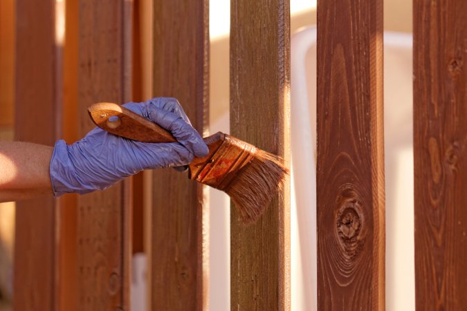 A person wearing rubber gloves is staining a wooden fence.