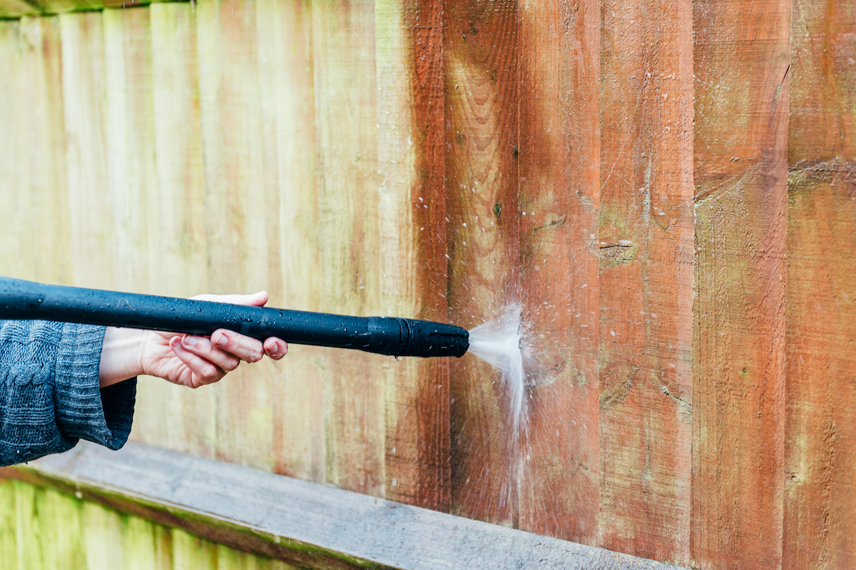 A person is using a power water to clean a wooden fence.