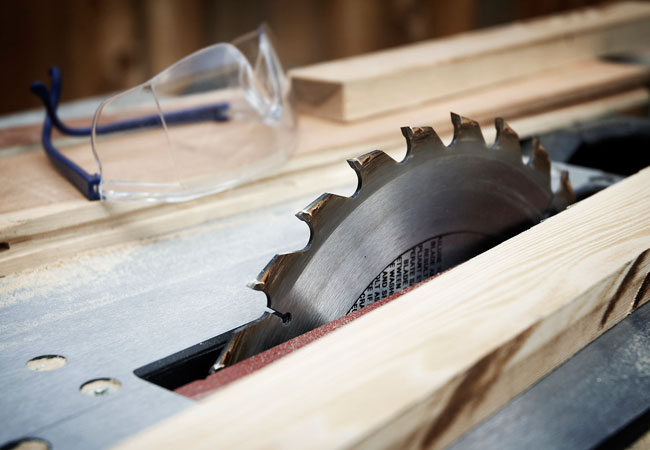 Close up view of a table saw blade next to a pair of safety glasses.