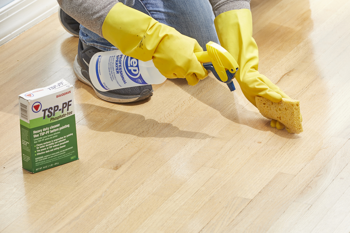 Woman wearing rubber gloves sprays a TSP solution on a hardwood floor.