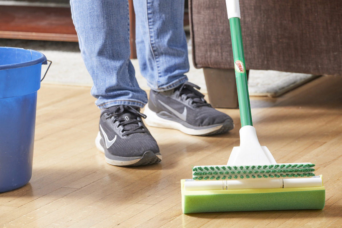 Woman uses a sponge mop and bucket to clean hardwood floors.