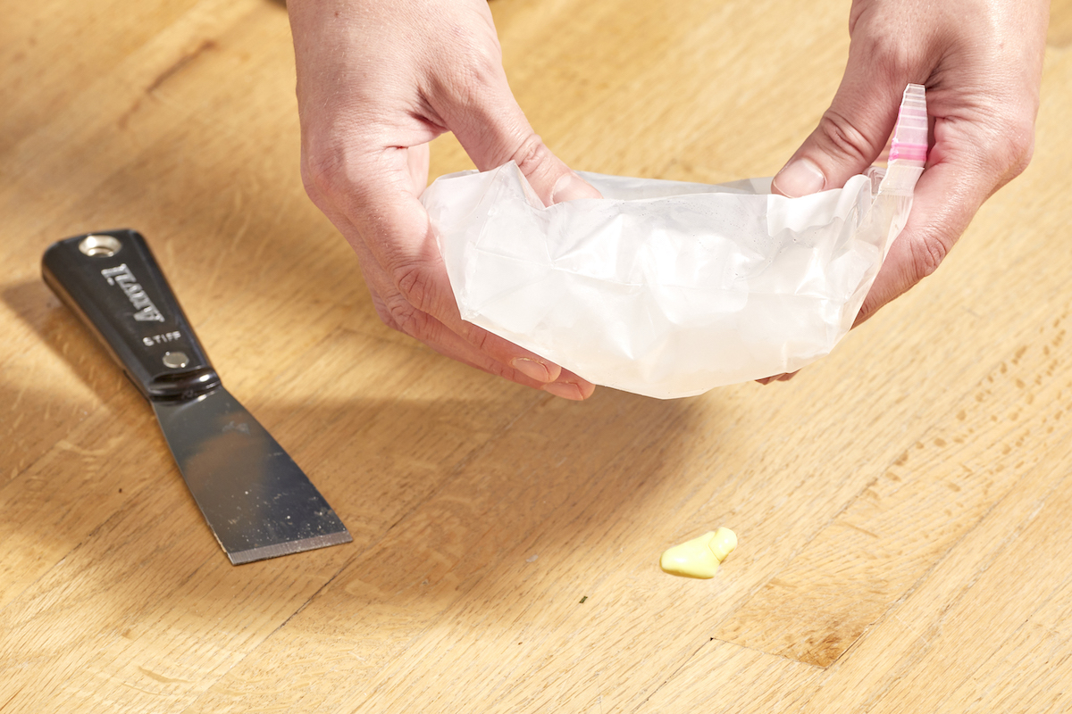 Woman applies a Ziploc bag with ice to wax on a hardwood floor.