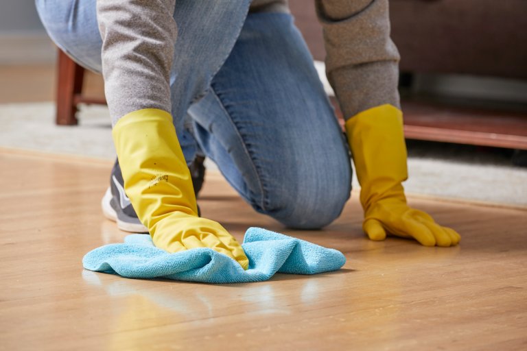 Woman wipes a hardwood floor with a blue microfiber cloth.