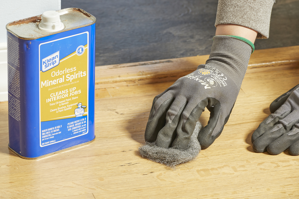 Woman uses steel wool to scrub mineral spirits into a hardwood floor.