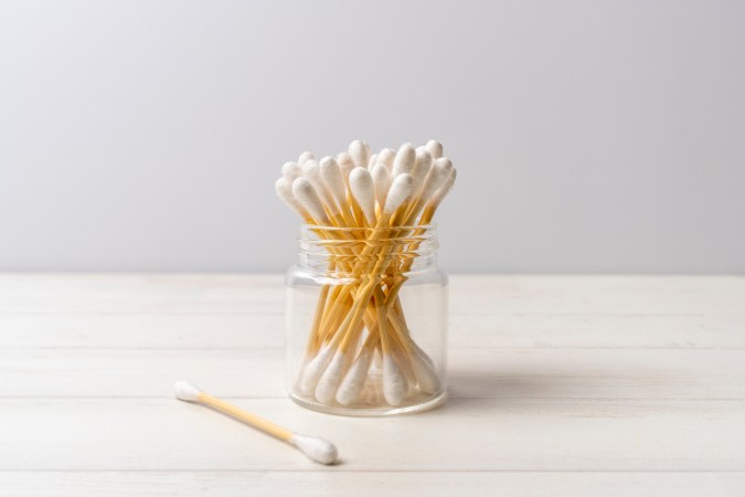 Front view of glass jar full of cotton swabs on a wooden background