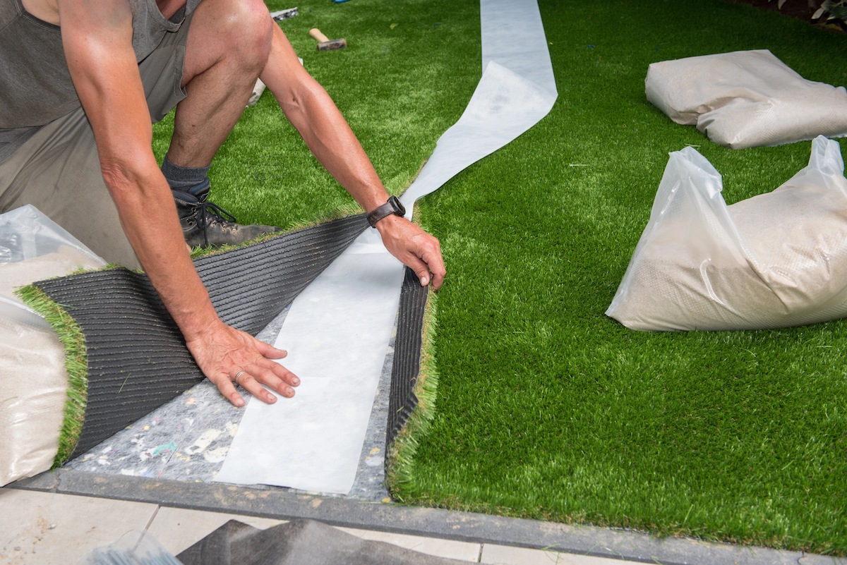 Gardener joins two strips of artificial grass with adhesive strip underneath.