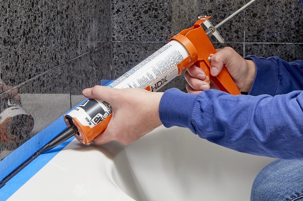 A person using a caulk gun to caulk around a shower and bathtub.