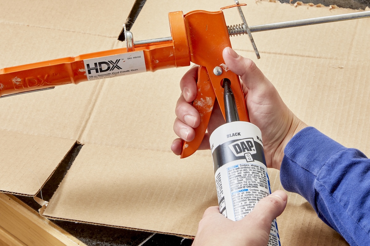 A person using a caulk gun to gut open a tube of caulk.