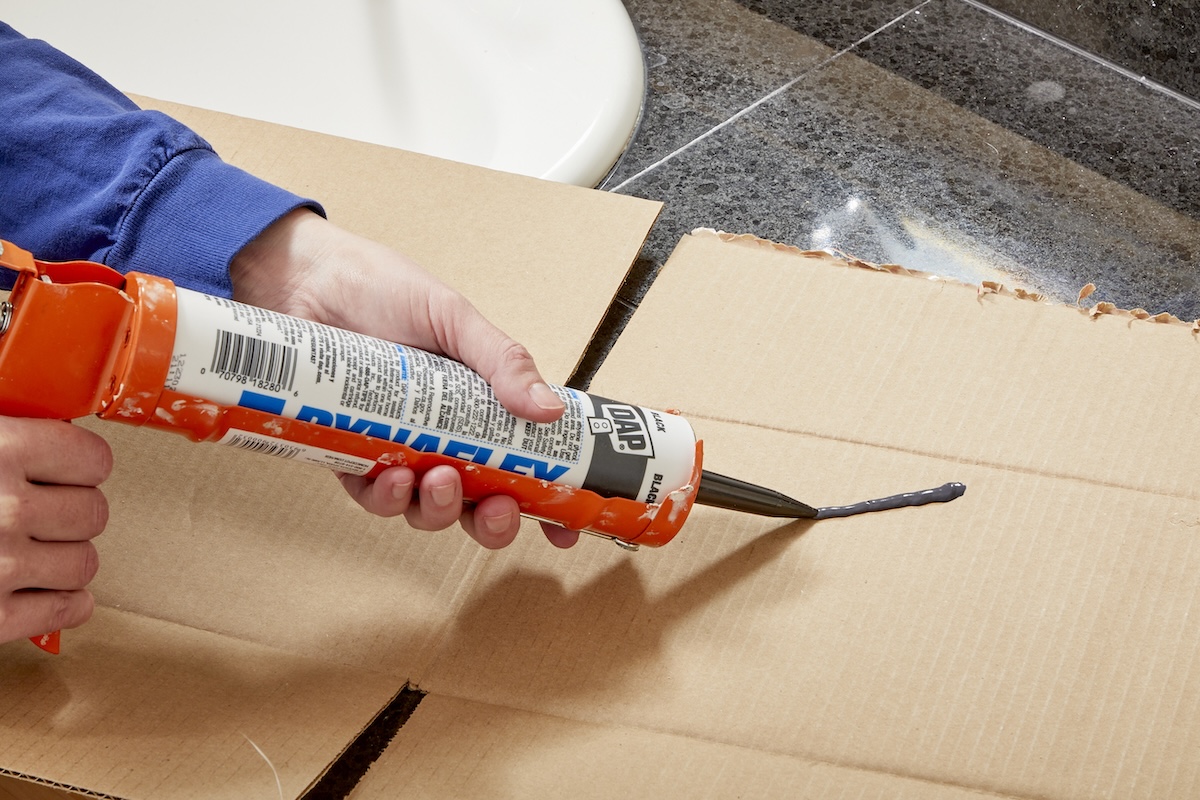 A person learning how to use a caulk gun before applying new caulking around a shower and bathtub.