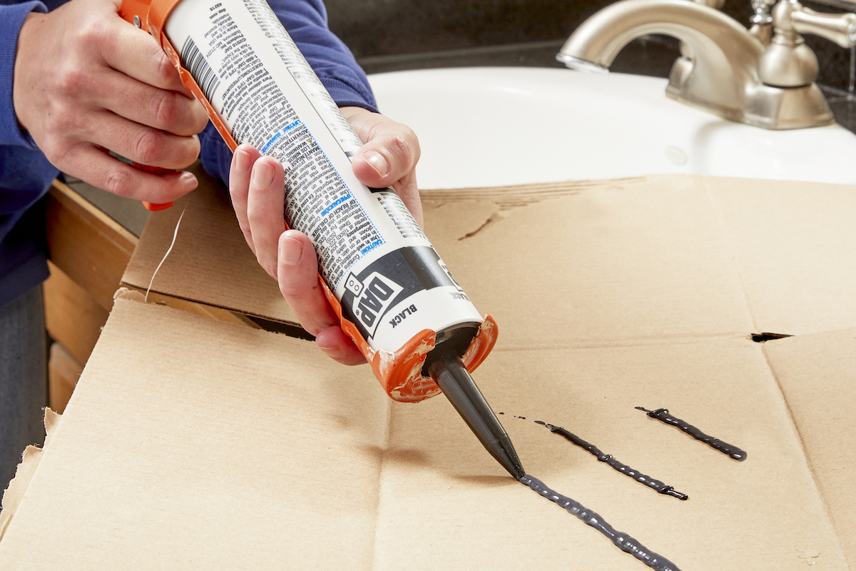 Woman tests a caulk gun on cardboard to make sure caulk is coming out.