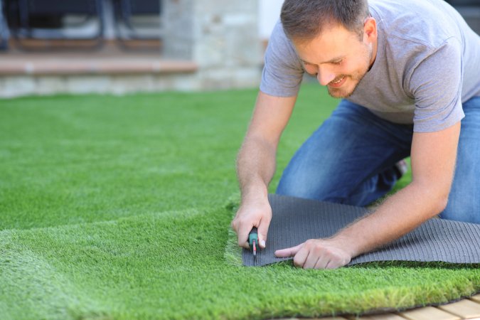 Happy man installing artificial lawn at home