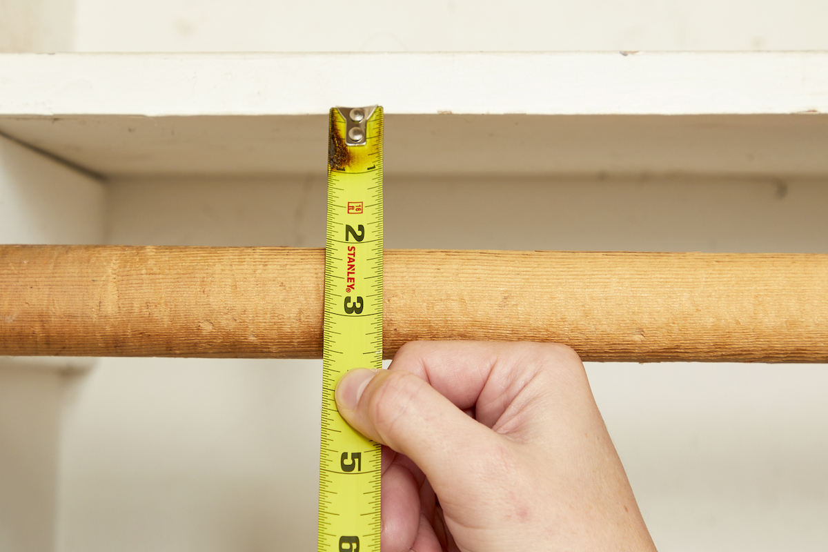 Tape measure shows a 3-inch distance between a high closet shelf and the middle of a closet rod.