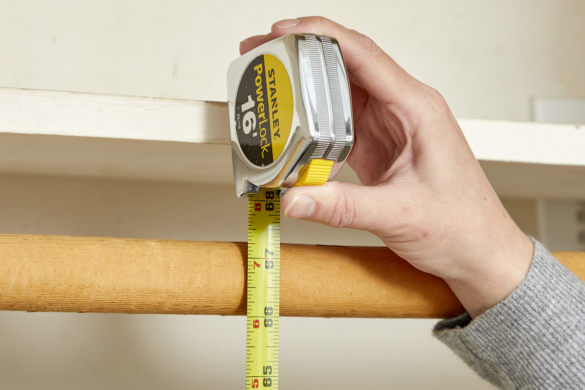 Woman measures the height of a closet rod with a tape measure that reads 66 inches at the bottom of the rod.