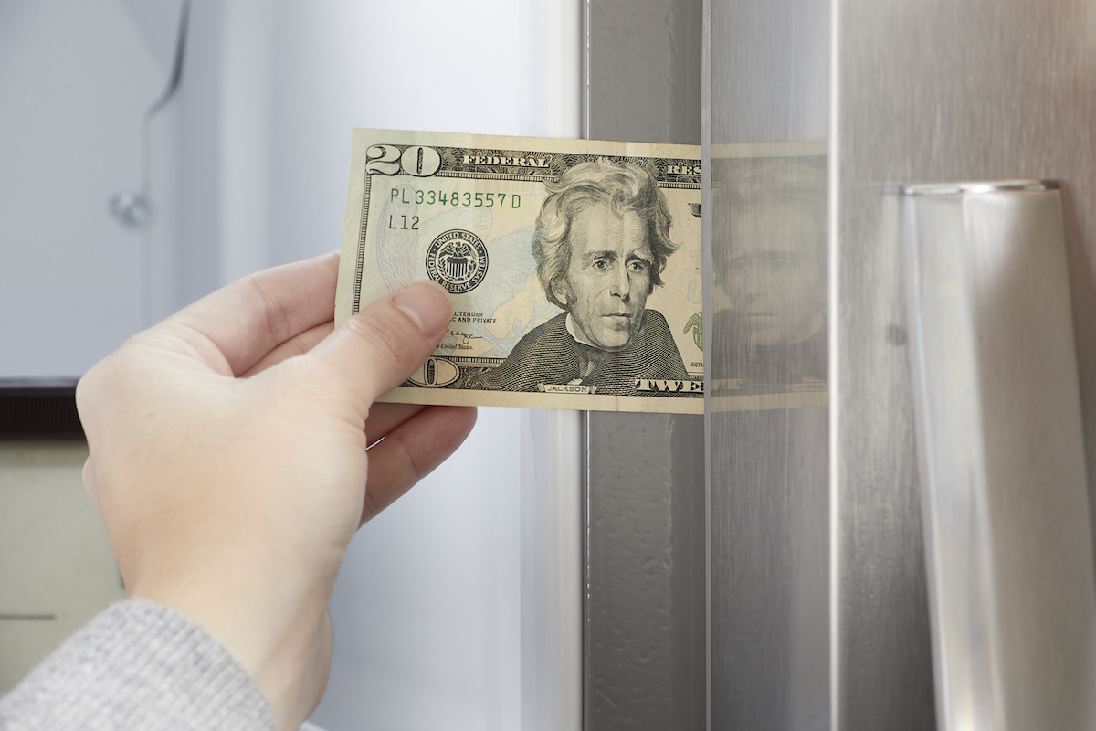 Woman puts a 20-dollar bill into the door gasket of a refrigerator.