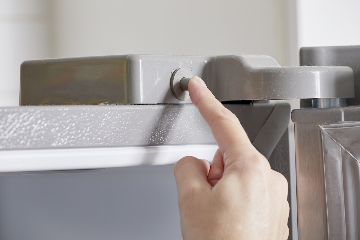 Woman pushes the button a refrigerator door  to test the appliance for power.