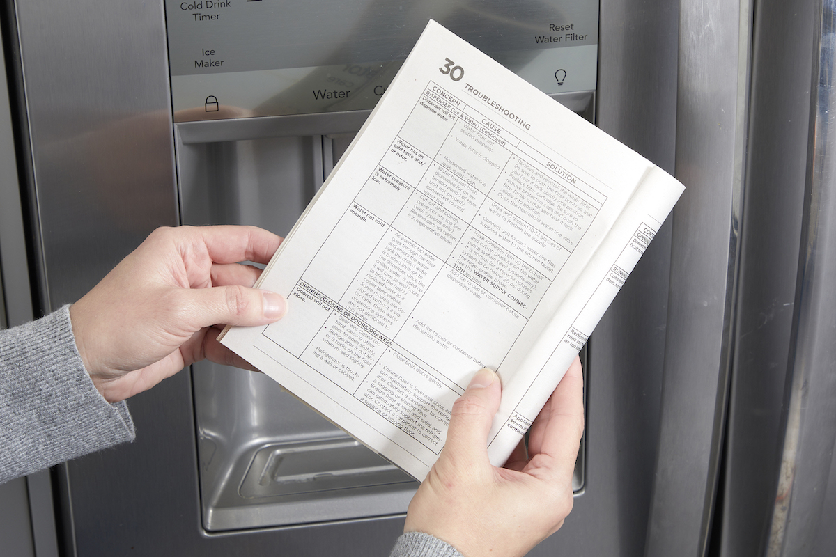 Woman reads the troubleshooting page of a refrigerator owner's manual.