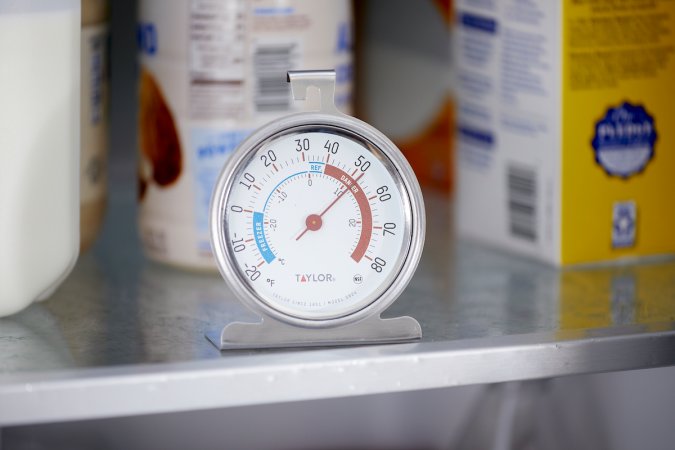 Small dial thermometer set on a refrigerator shelf.