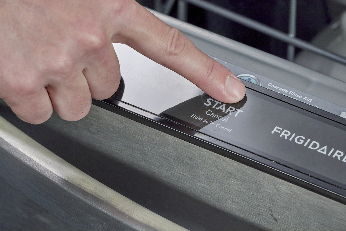 Woman presses the "start/cancel" button on her dishwasher control panel.