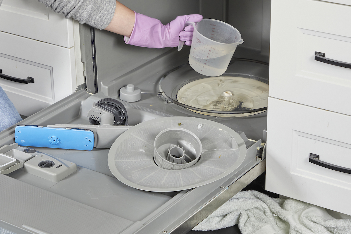 Woman uses a measuring cup to scoop water out of the bottom of a dishwasher.