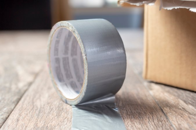 Roll of duct tape with end taped to a wood table, a cardboard box next to the tape.