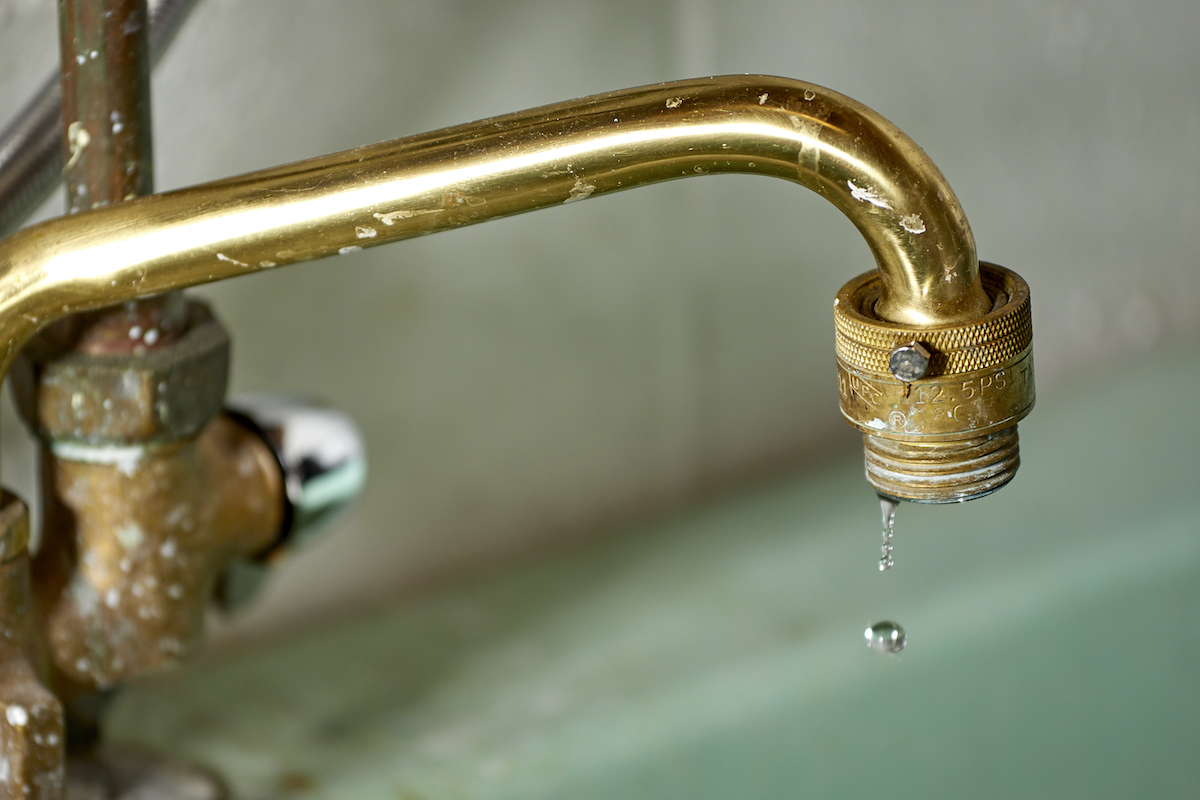 Laundry sink faucet drips into a light green sink.