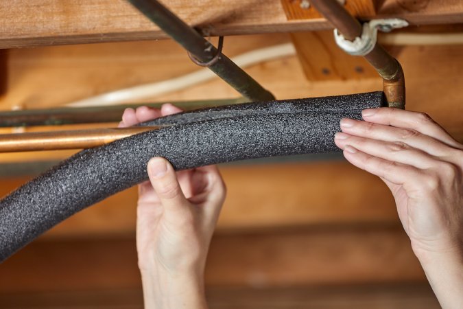 Person putting pipe insulation on a copper basement pipe.