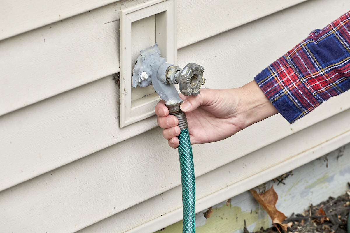 Woman disconnects garden hose from outdoor spitgot on house.