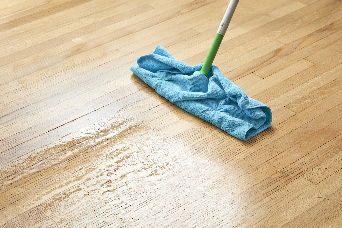 A dry mop wrapped in a microfiber cloth is being used to clean hardwood floors.