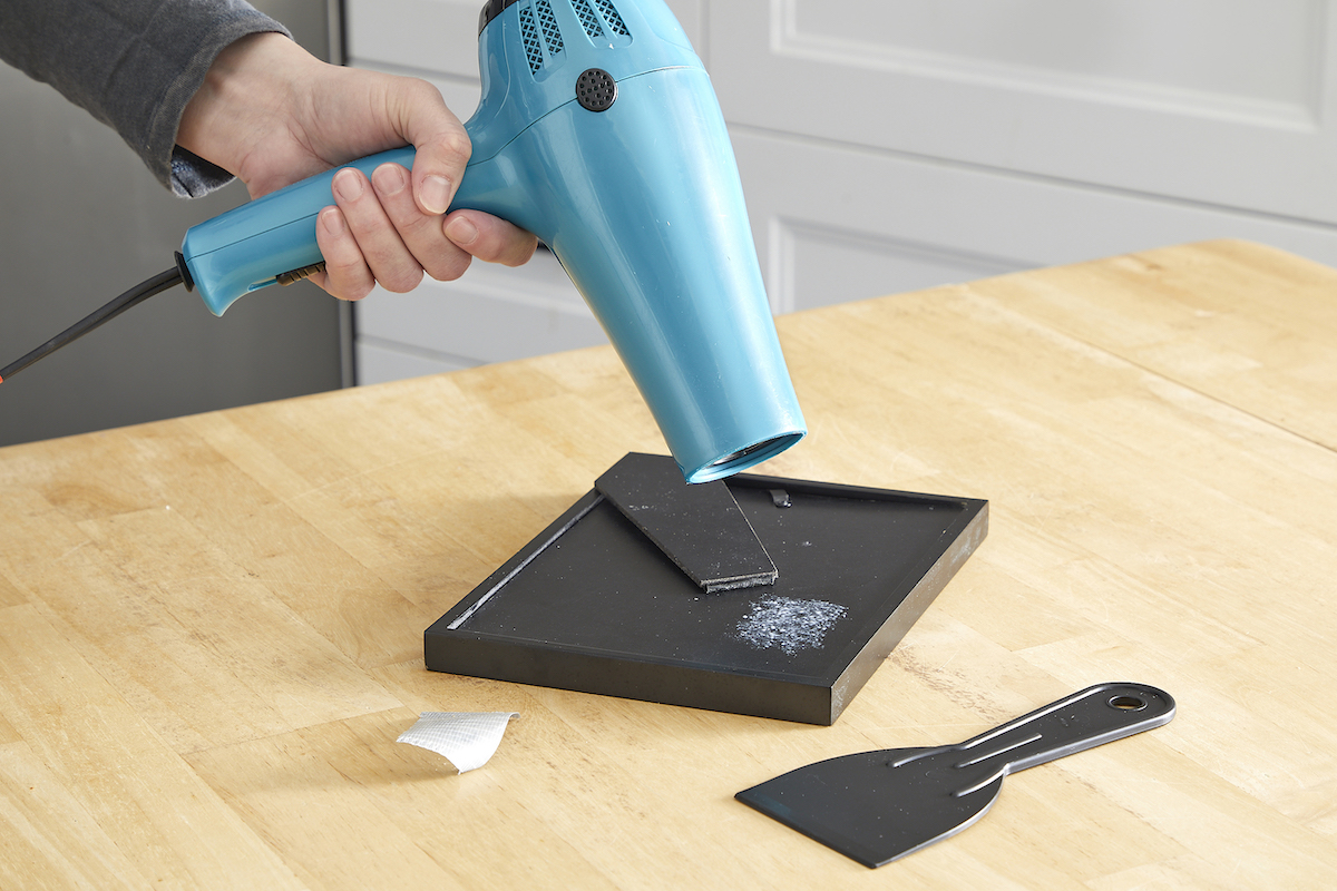 Person uses hair dryer to heat duct tape residue on a photo frame.