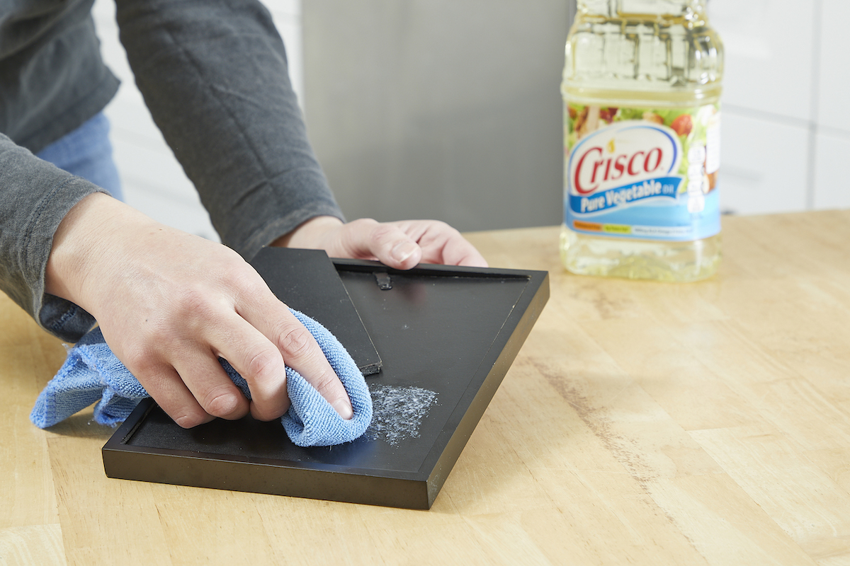 Woman uses cooking oil to moisten duct tape residue on a photo frame.