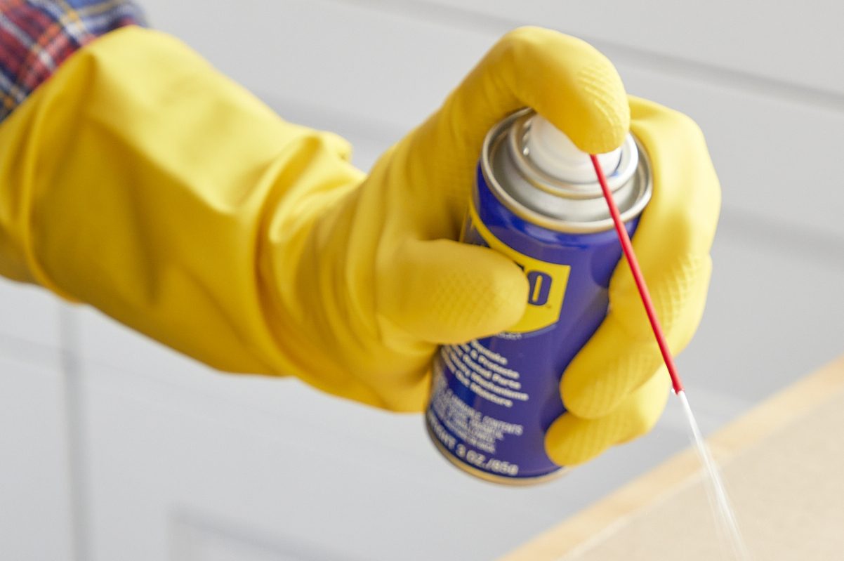 Person wearing yellow rubber gloves points stream of WD40 downward.