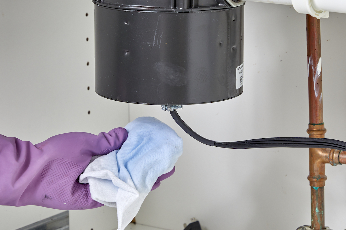 Person with rubber gloves holds white cloth with blue water stain under a garbage disposal.