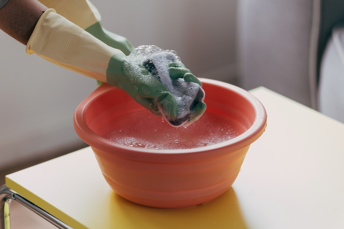 Close-up of gloved hands washing a rag in soapy water.