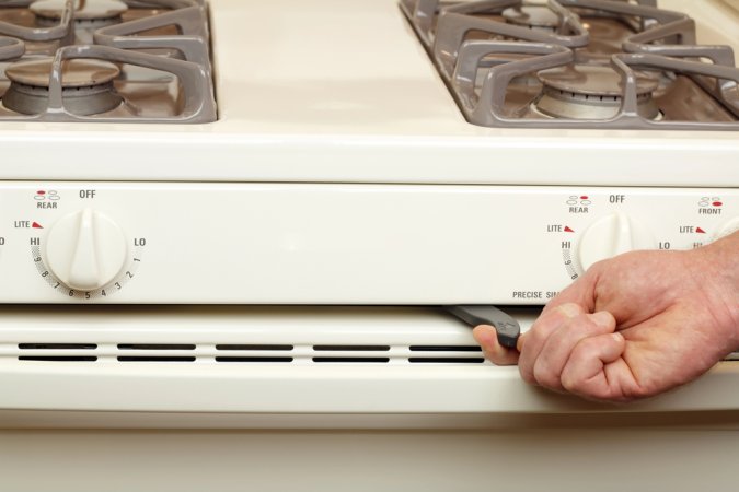 Hand turning on self-clean function on white oven.