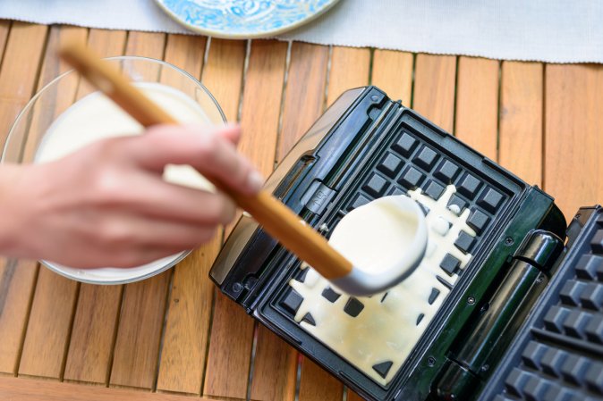 Preparation of homemade waffles. Pouring dough into waffle irons with a ladle