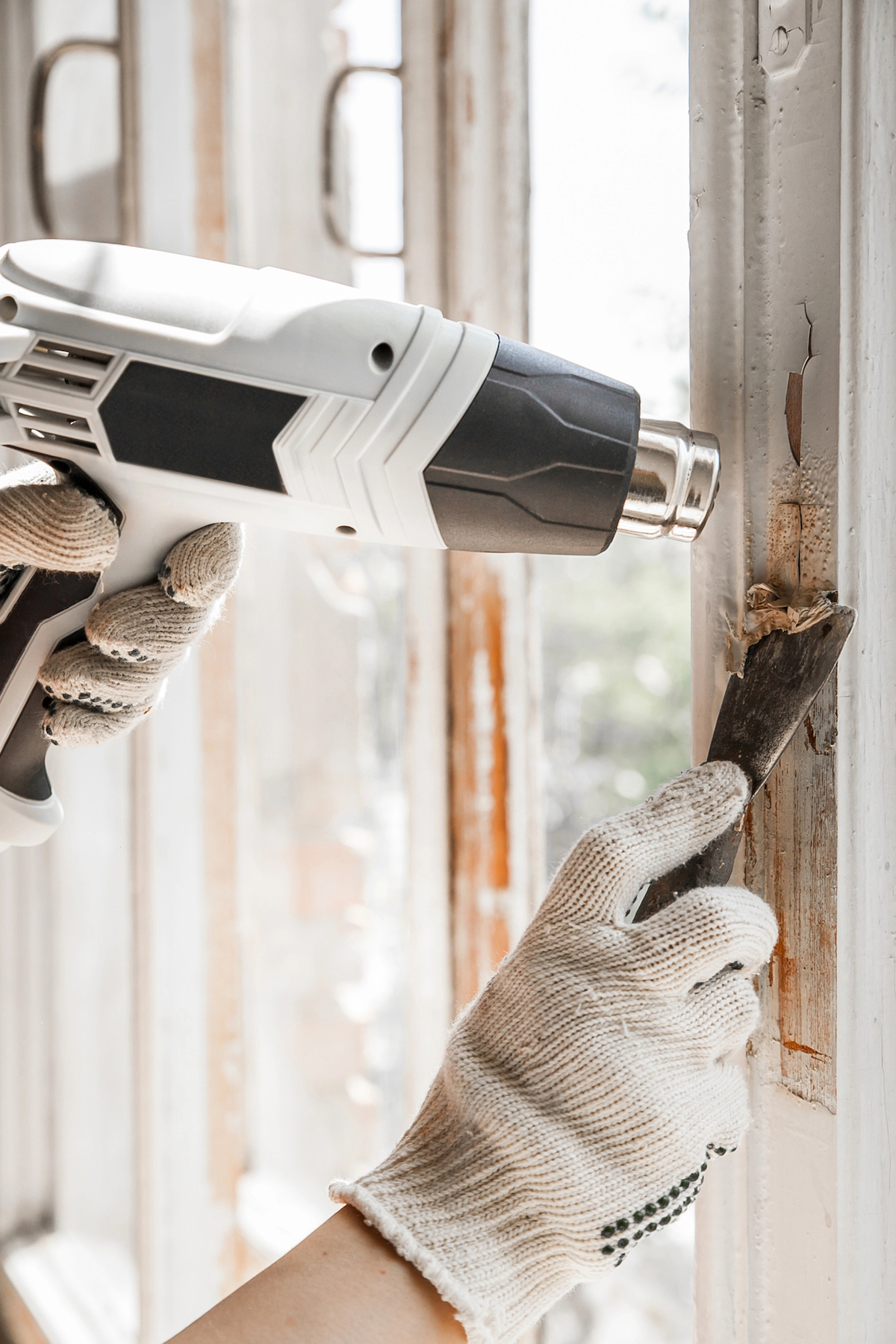 A person wearing gloves is using a heat gun and scraper tool to remove excess epoxy.