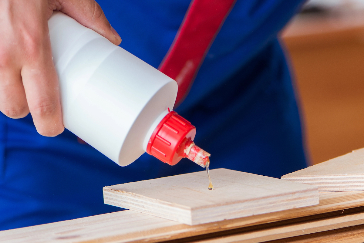 A person is squeezing epoxy glue from a bottle onto a square piece of wood.