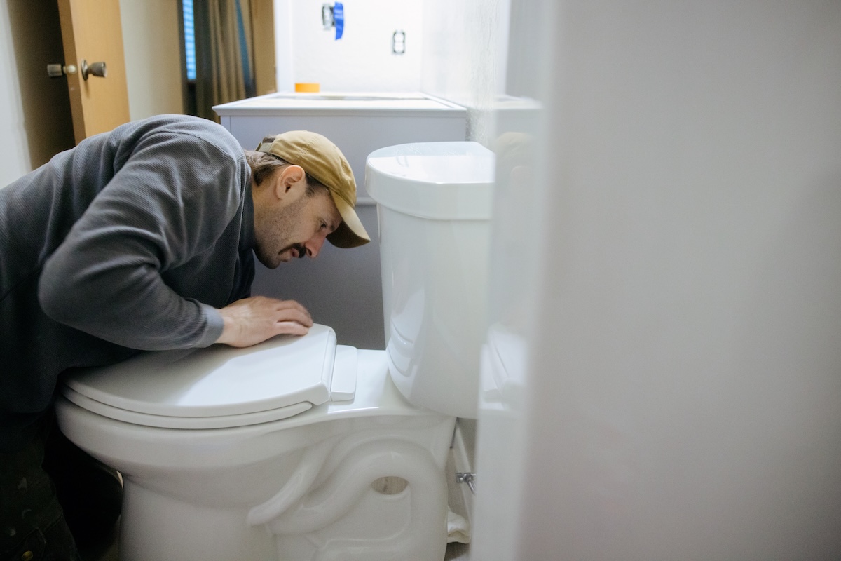 A man in a hat inspects a broken toilet.