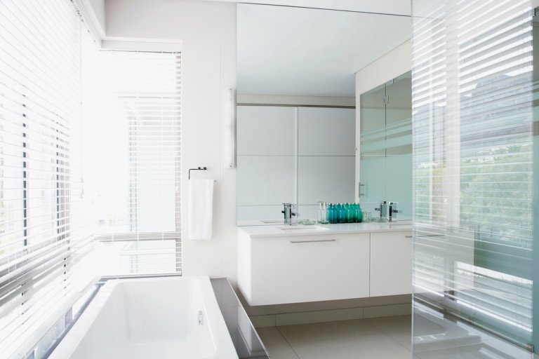 An airy, modern bathroom with a very large mirror going from ceiling to the top of a modern white sink.