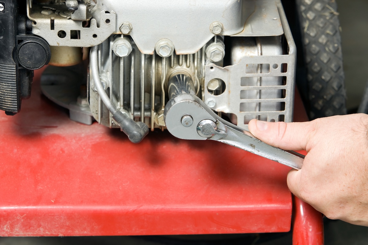 A repairperson removes spark plugs from a small red engine.