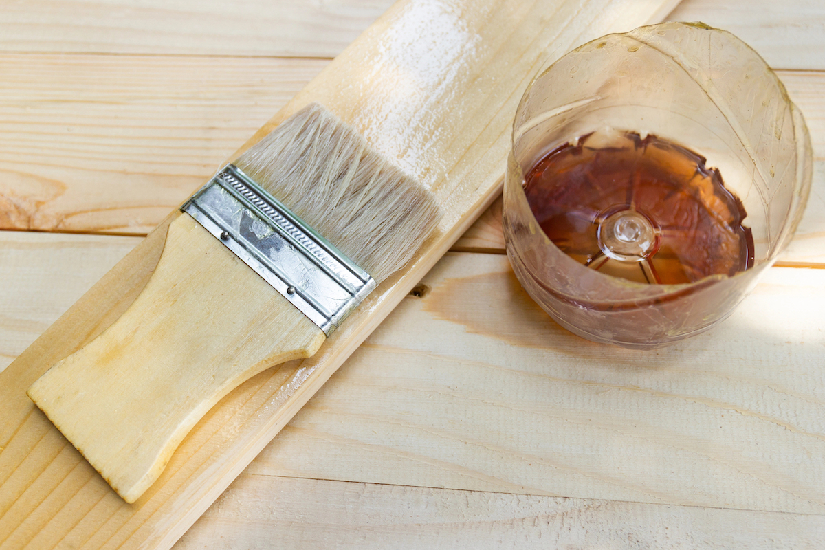 Shellac in a plastic bowl, small paintbrush, and a scrap of wood.