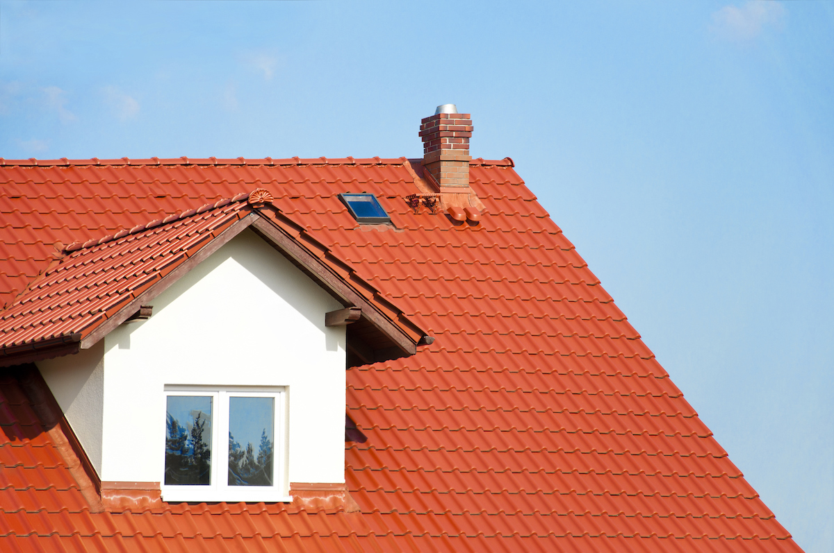 Close-up of red roof tiles, brick chimney and dormer window.