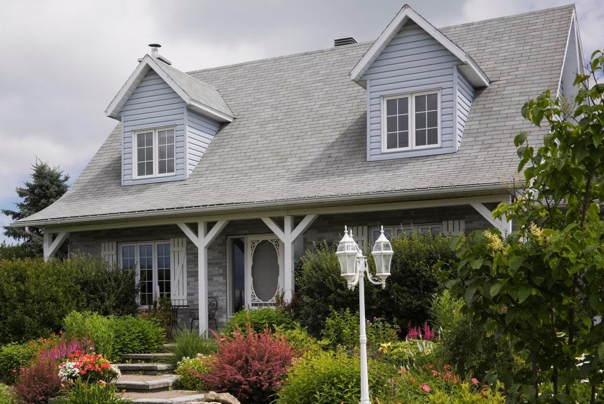 Old grey nuanced brick with white trim cottage style Canadiana home facade with landscaped front yard in summer, Quebec, Canada. This image is property released. CUPR0285