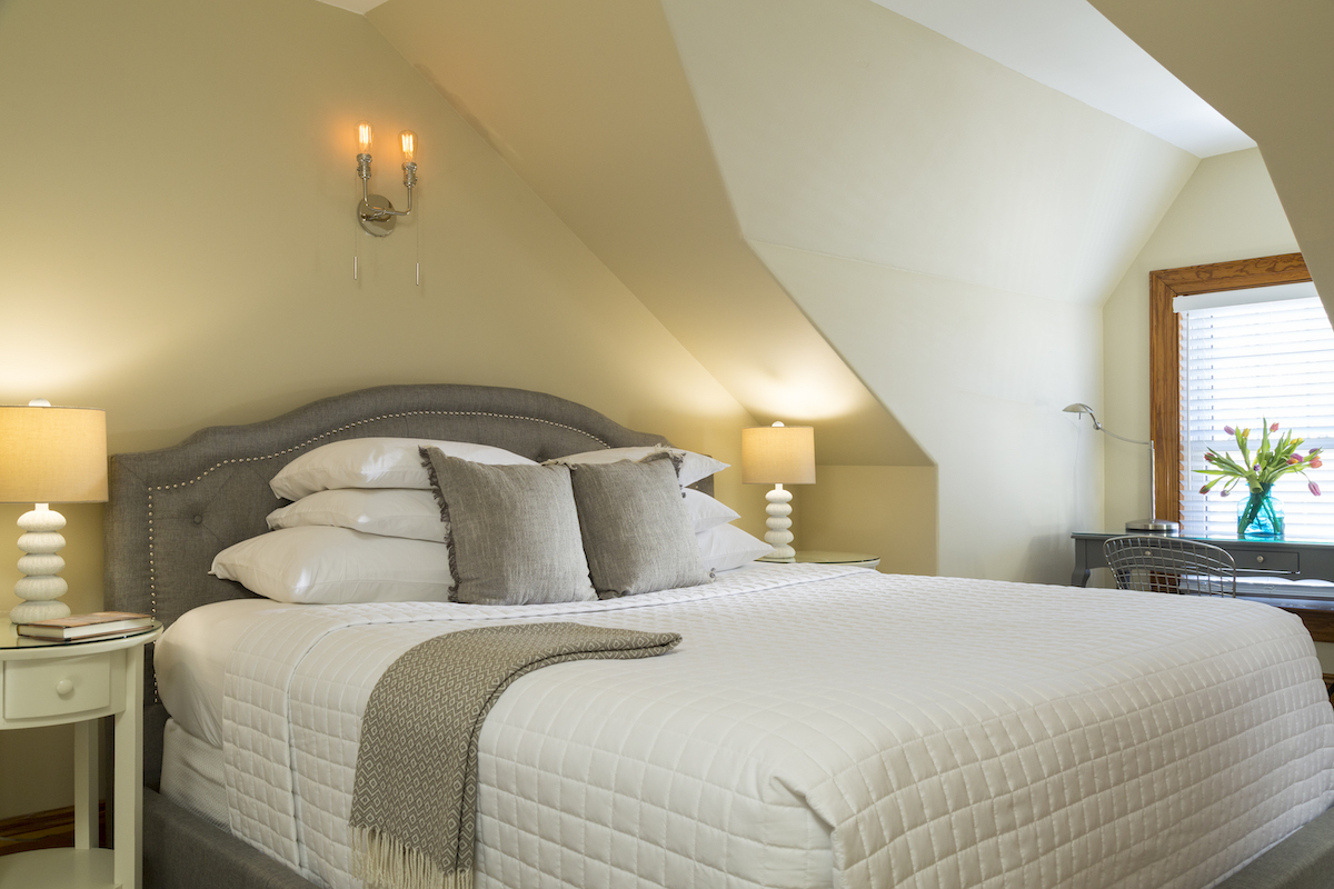 Bed and lamp in a modern interior with a dormer window, flooded with sunlight.