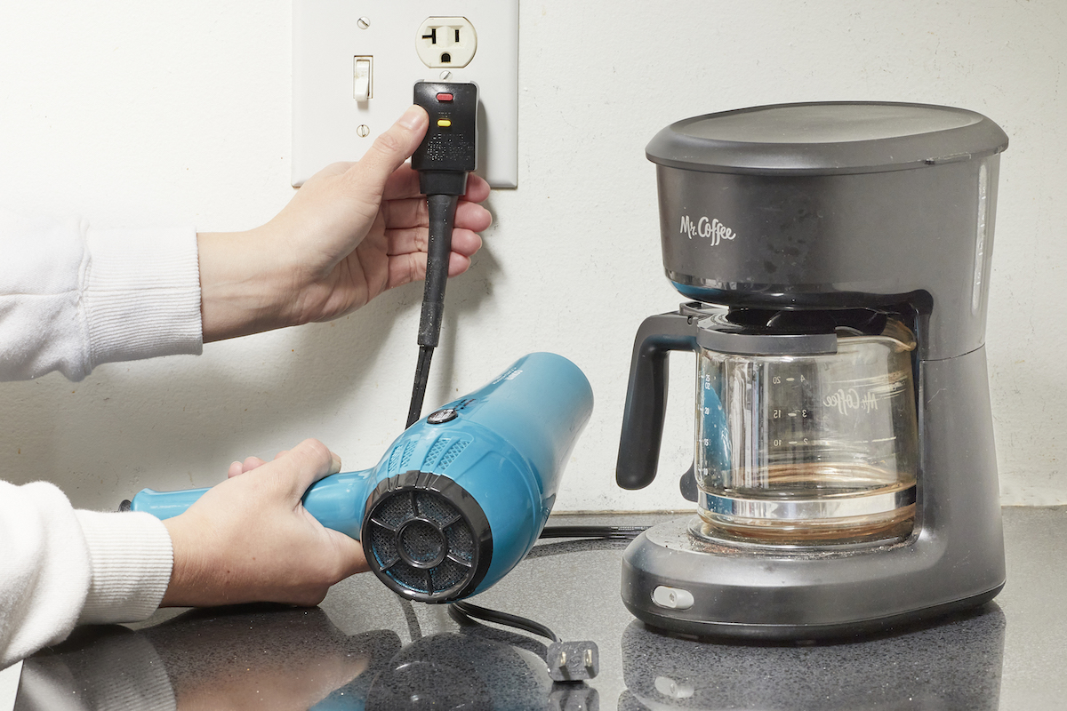 Woman unplugs coffee maker in kitchen and plugs hair dryer in same outlet.