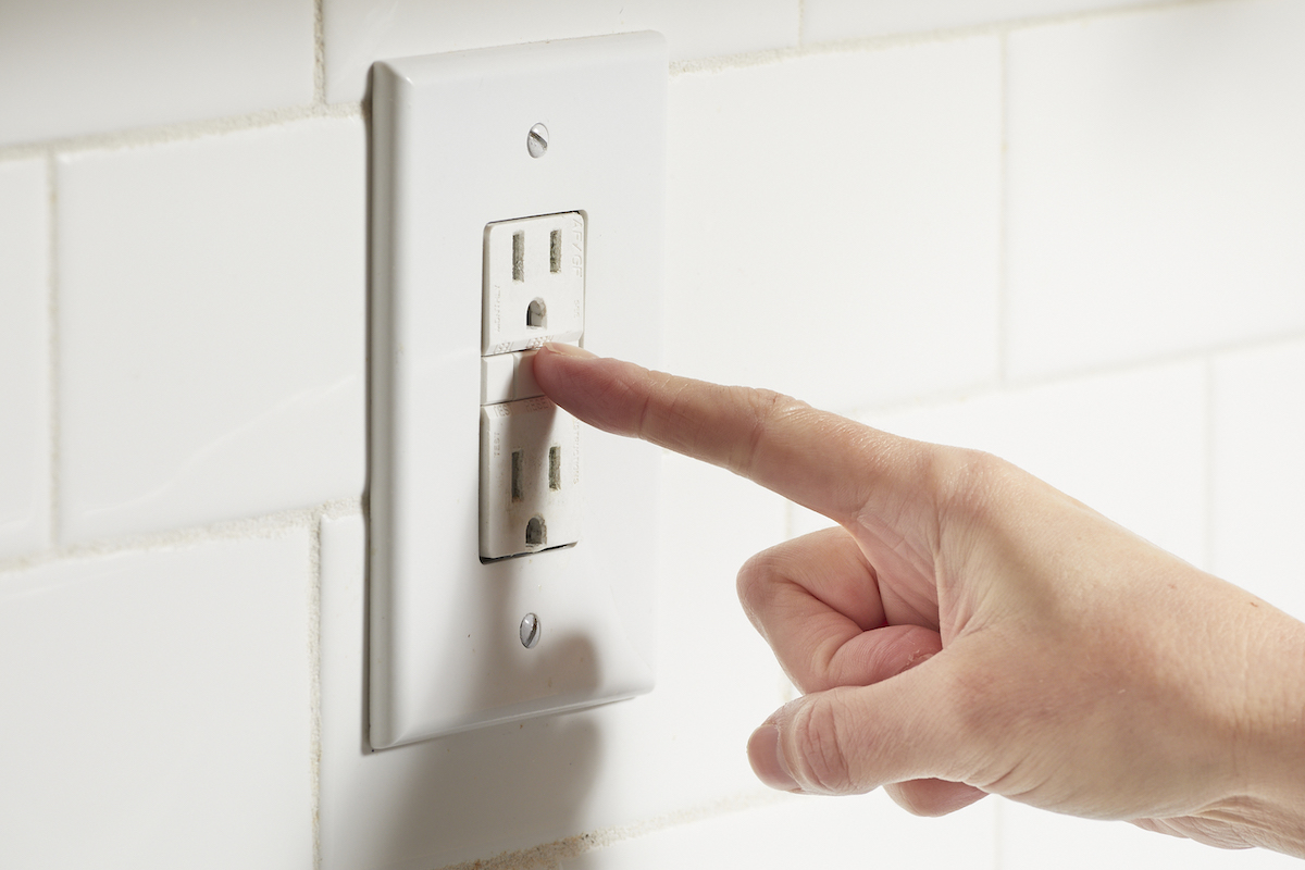 Woman pushes the reset button on a GFCI outlet surrounded by white subway tile.