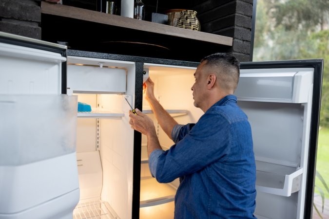 A man fixes a broken refrigerator.