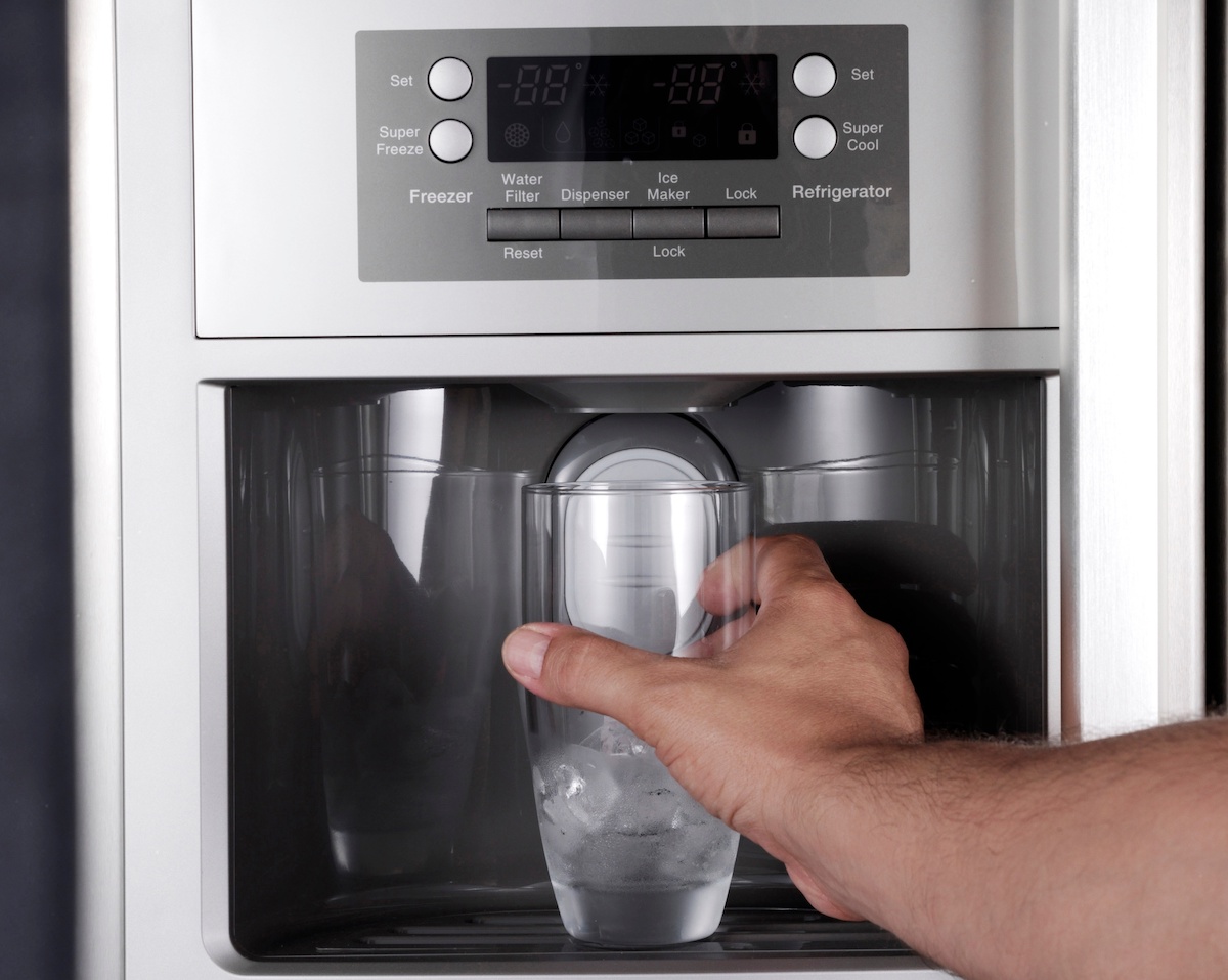 Person putting a glass of ice under the water dispenser on a stainless steel refrigerator.