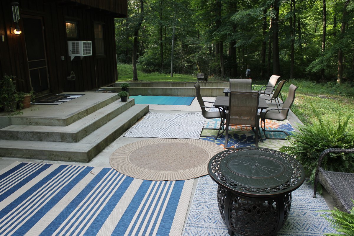 Five of the Best Outdoor Rugs on a concrete patio surrounded by trees